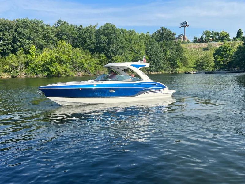 Slide: The Image of 2023 Formula 310 Bowrider I/O boat cruising on a scenic lake with lush green trees. - 25