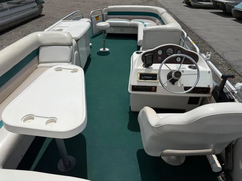 Slide: The Image of 1999 AquaPatio 270fe pontoon boat interior with green carpet, white seating, and steering console. - 23