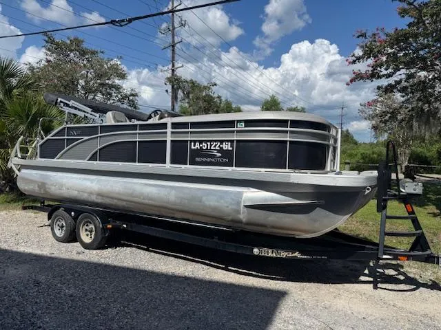 Slide: The Image of 2020 Bennington SX22 pontoon boat on trailer, parked outdoors under a partly cloudy sky. - 2