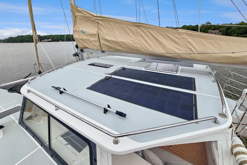 Slide: The Image of 2018 Maine Cat 38 LS sailboat with solar panels on deck, docked by a scenic shoreline. - 32