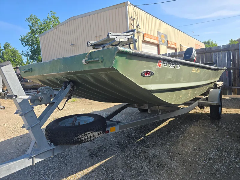 Slide: The Image of Green Custom Flat 16 boat on trailer, parked outside a garage, 2016 model. - 2