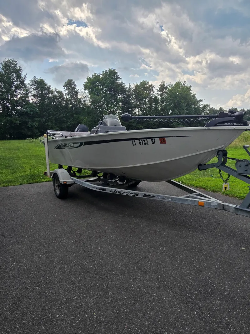 Slide: The Image of 2012 Lowe AN160S boat on trailer, parked on asphalt near grassy area. - 2