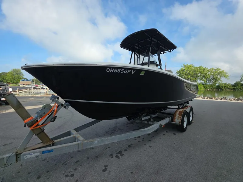 Slide: The Image of 2018 NauticStar 22 XS Offshore boat on trailer, parked near water under blue sky. - 2
