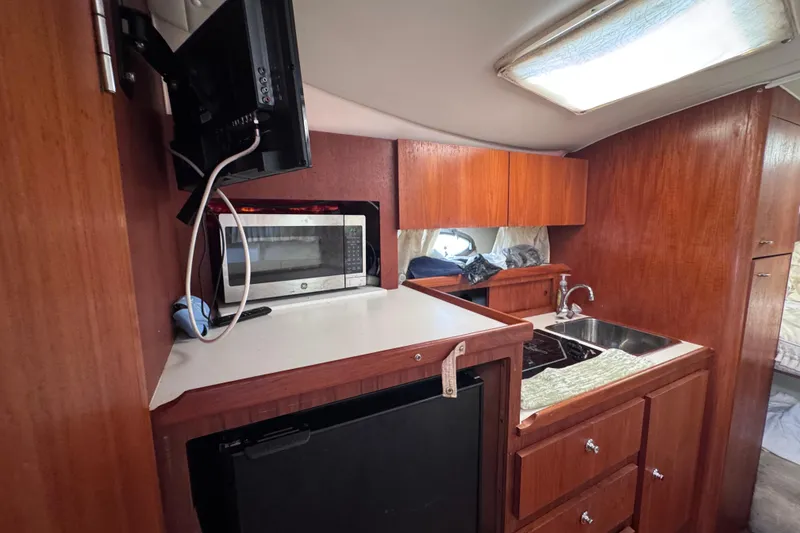 Slide: The Image of 2001 Tiara Yachts 3100 Open interior with kitchenette, featuring microwave, sink, and wooden cabinetry. - 39