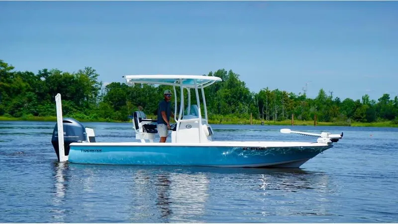 Slide: The Image of 2023 Tidewater 2110 Bay Max boat on calm water with lush green background. - 1