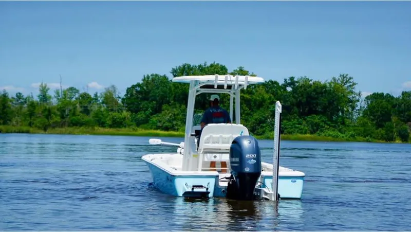 Slide: The Image of 2023 Tidewater 2110 Bay Max boat cruising on a calm lake with trees in the background. - 2