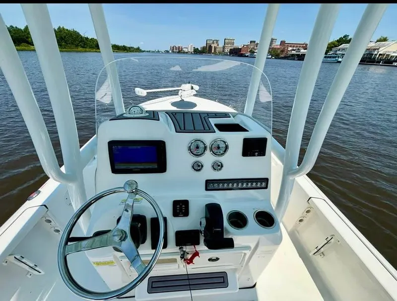Slide: The Image of 2023 Tidewater 2110 Bay Max boat dashboard with steering wheel and controls on a river. - 8