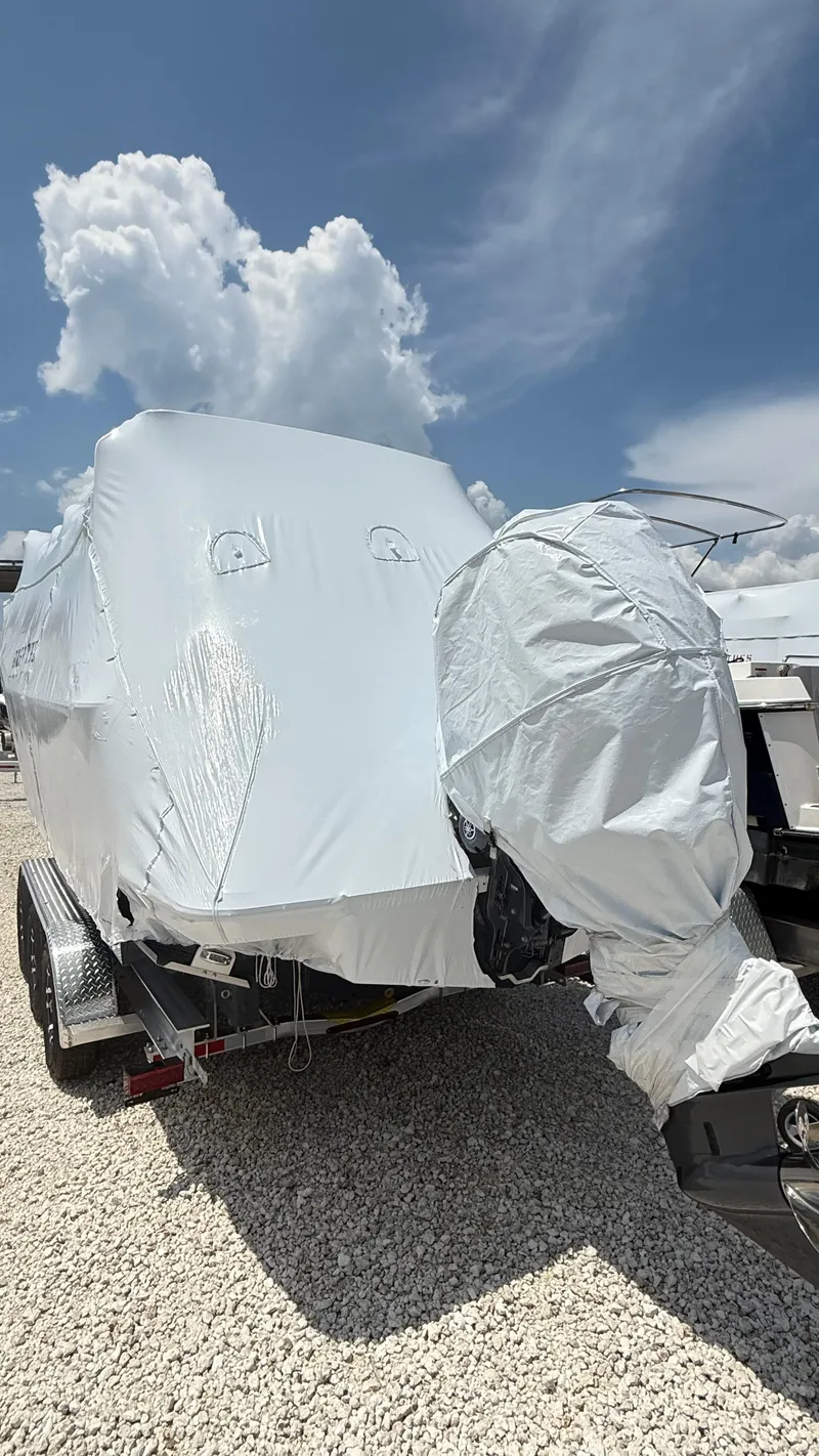 Slide: The Image of 2026 Ranger Tugs R-27 boat covered in protective wrap on a trailer, under a cloudy sky. - 2