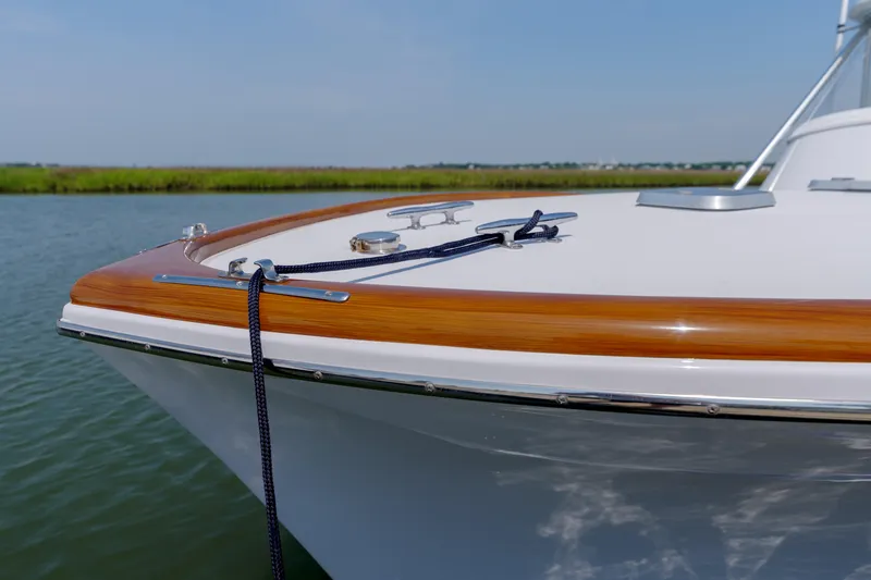 Slide: The Image of 1998 Gamefisherman Enticer boat bow with polished wood trim and mooring line on calm water. - 29