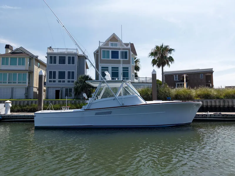 Slide: The Image of 1998 Gamefisherman Enticer boat docked near waterfront homes, under a clear blue sky. - 3