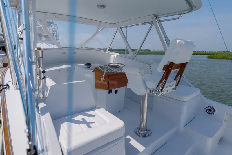 Slide: The Image of 1998 Gamefisherman Enticer boat helm with white seating and steering wheel, docked by calm waters. - 7