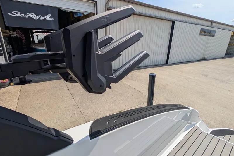 Slide: The Image of 2025 Sea Ray SLX 260 Surf boat with advanced wakeboard rack, docked near a marine shop. - 27