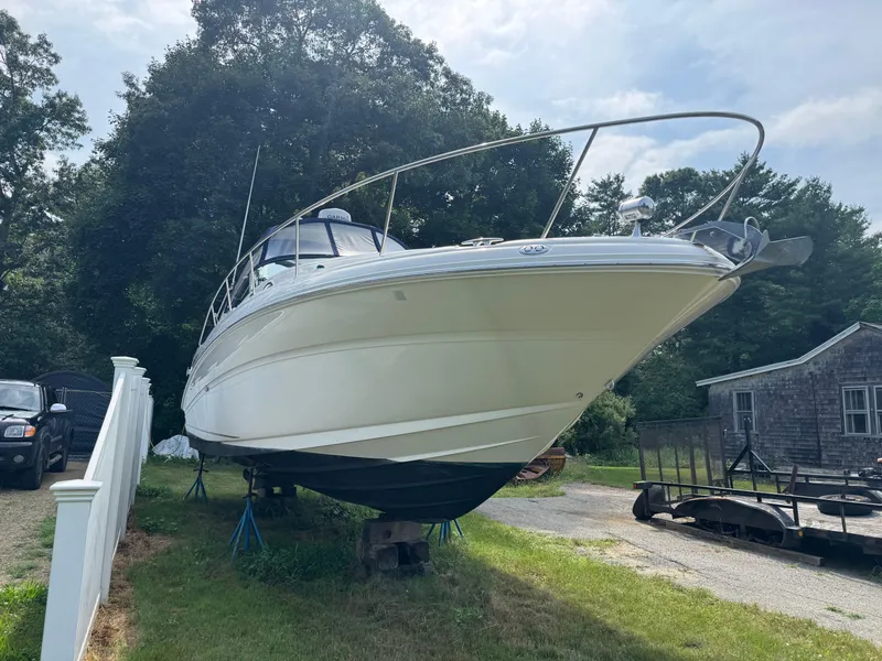 Slide: The Image of 2003 Sea Ray 320 Sundancer boat on stands, parked outdoors near trees and a house. - 16