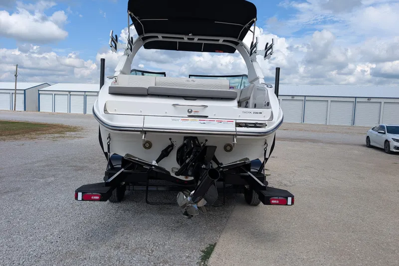 Slide: The Image of 2026 Sea Ray SDX 230 Surf boat rear view in storage lot, under cloudy sky. - 8