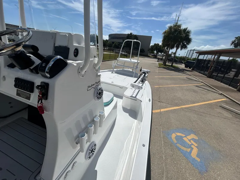 Slide: The Image of 2024 Shallow Sport 24 Modified V boat parked in a sunny lot near palm trees. - 12