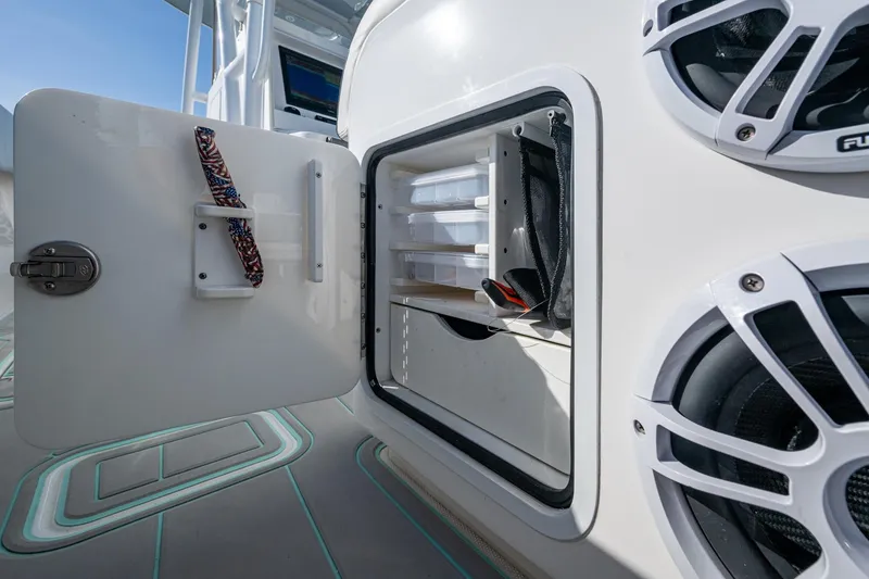 Slide: The Image of Open storage compartment on 2022 Invincible 33 Catamaran, featuring organized tackle boxes and speakers. - 35