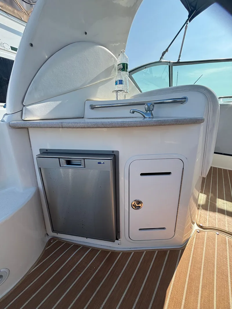 Slide: The Image of 2004 Sea Ray 320 Sundancer boat kitchenette with sink, mini fridge, and storage cabinet. - 19