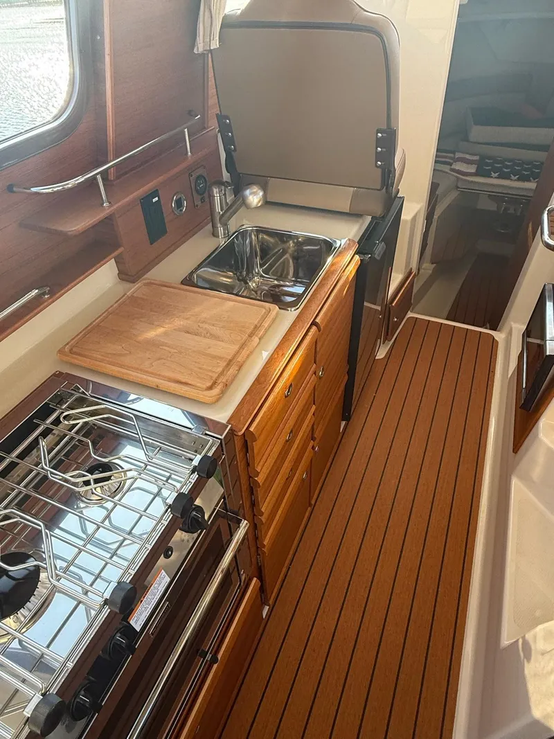 Slide: The Image of 2023 Ranger Tugs R-27 interior kitchen with stove, sink, and wooden cabinetry. - 13