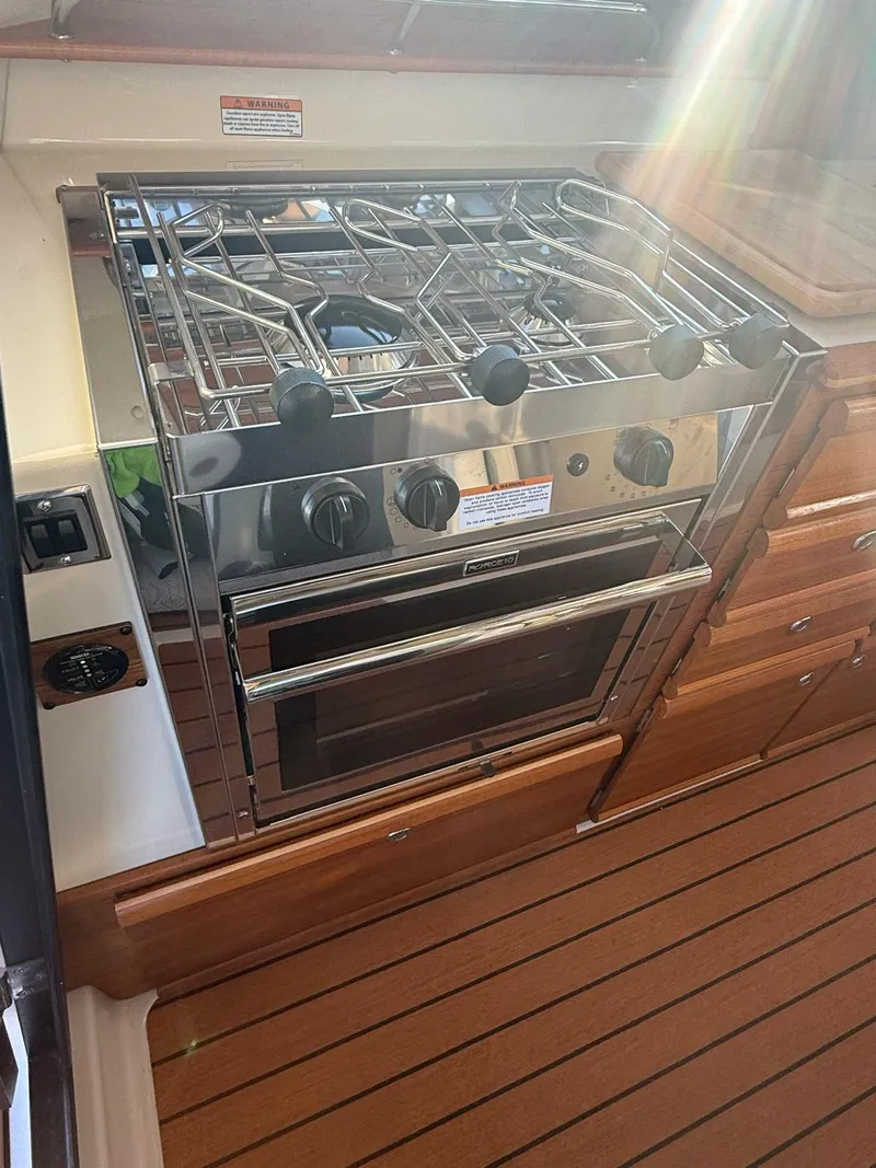 Slide: The Image of 2023 Ranger Tugs R-27 boat kitchen with stainless steel stove and wooden cabinetry. - 14