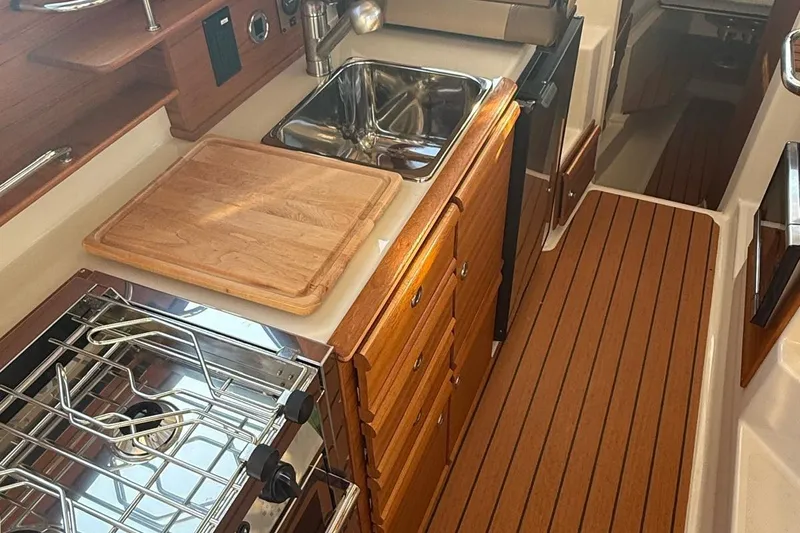 Slide: The Image of 2023 Ranger Tugs R-27 galley with stove, sink, and wooden cabinetry. - 18
