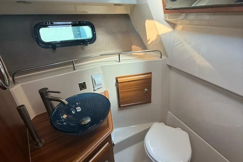 Slide: The Image of 2023 Ranger Tugs R-27 bathroom with modern sink, toilet, and porthole window. - 21