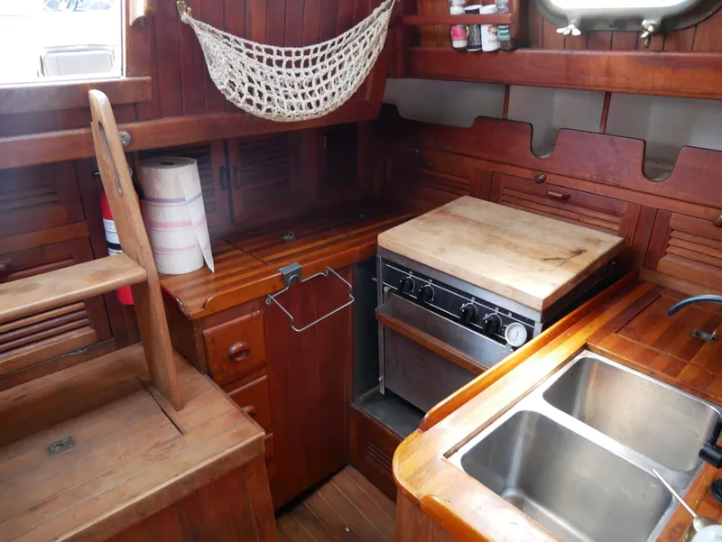 Slide: The Image of 1978 Baba 30 sailboat galley with wooden cabinetry, stove, sink, and storage shelves. - 16