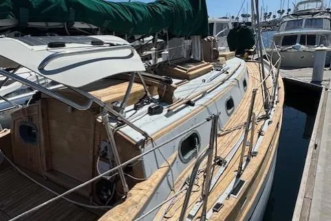 Slide: The Image of 1978 Baba 30 sailboat docked, featuring wooden deck and green sail cover. - 4