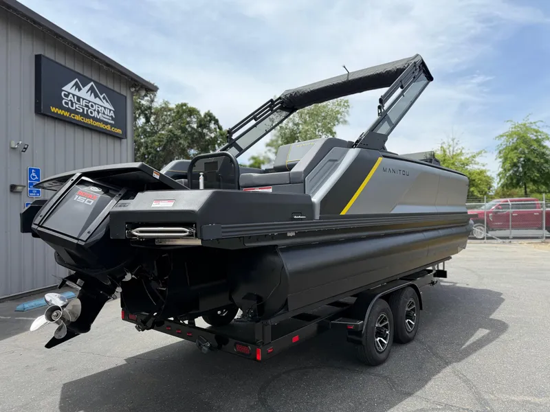 Slide: The Image of 2025 Manitou Explore boat on trailer at California Custom dealership. - 5