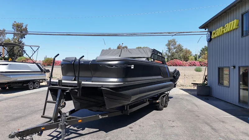 Slide: The Image of 2025 Manitou Explore Dual Engine boat on trailer near Can-Am building. - 5