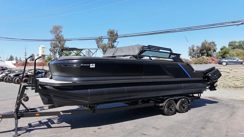 Slide: The Image of 2025 Manitou Explore Dual Engine boat on trailer, parked outdoors. - 6