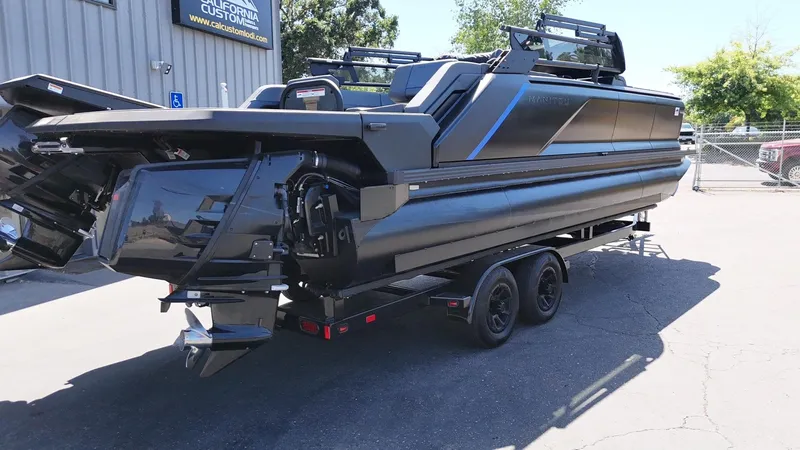 Slide: The Image of 2025 Manitou Explore Dual Engine boat on trailer, parked outdoors. - 7