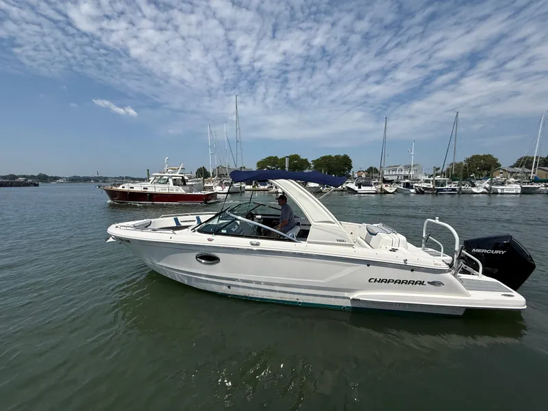 The Image of 2022 Chaparral 267 SSX OB boat on calm water, with marina background. - 0