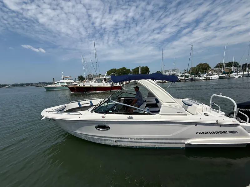 Slide: The Image of 2022 Chaparral 267 SSX OB boat on calm water, with marina and sailboats in background. - 2