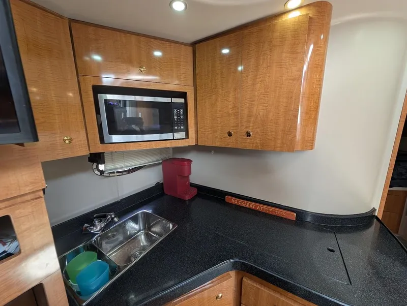 Slide: The Image of 2002 Regal Commodore 3860 yacht kitchen with microwave, sink, and wooden cabinets. - 26