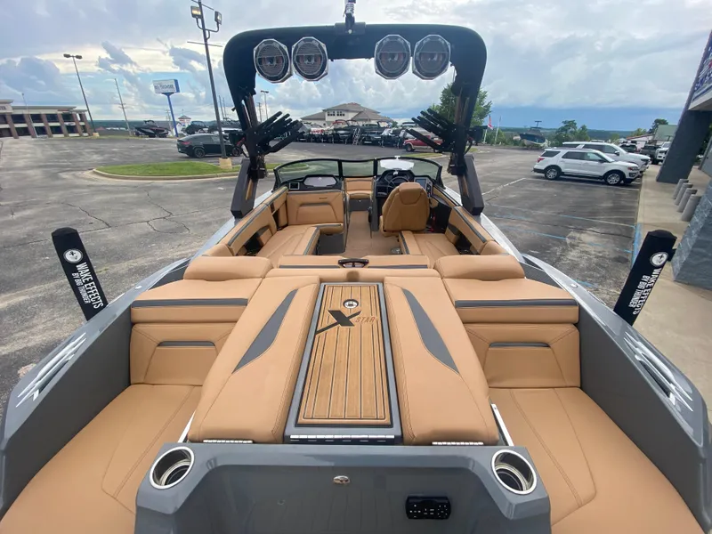 Slide: The Image of 2022 MasterCraft XStar boat with tan interior, parked in a lot under cloudy skies. - 2