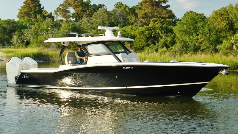 The Image of 2023 Scout 377 LXF boat cruising on a calm river with lush greenery. - 0