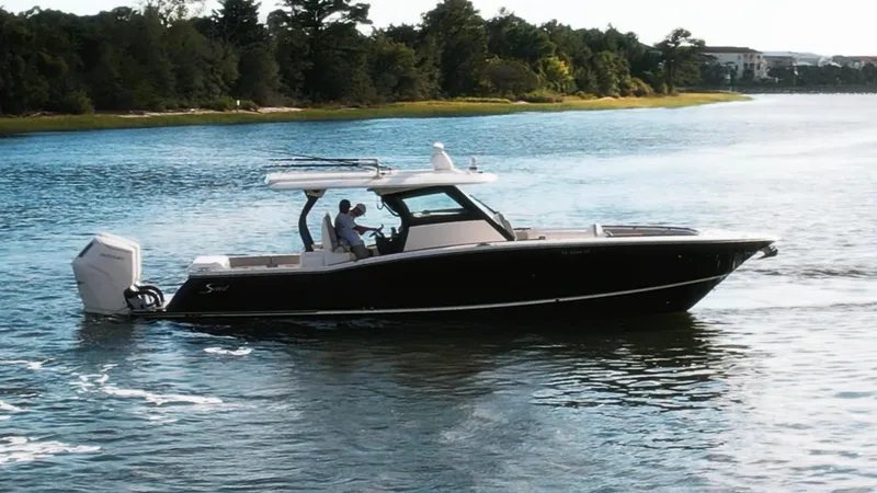Slide: The Image of 2023 Scout 377 LXF boat cruising on a serene lake with lush greenery. - 12