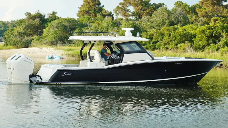 Slide: The Image of 2023 Scout 377 LXF boat cruising on a calm lake near a wooded shoreline. - 4