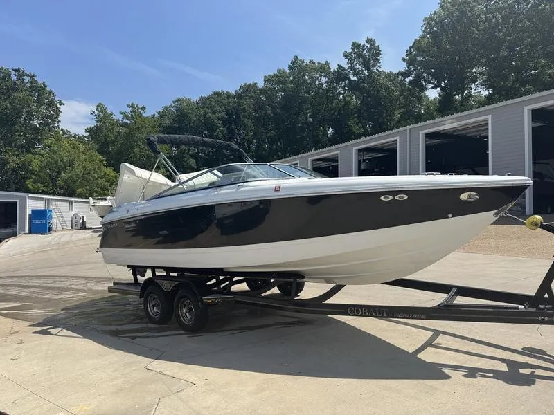 Slide: The Image of 2006 Cobalt 250 boat on trailer, parked near storage facility, surrounded by trees. - 6