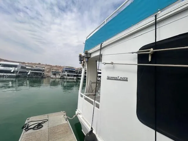 Slide: The Image of 1999 Skipperliner 59 x 14 houseboat docked on calm water, with clear sky. - 24