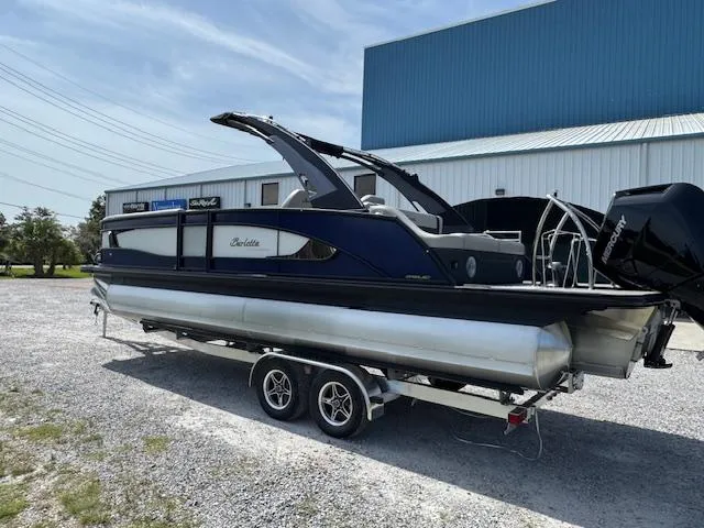 Slide: The Image of 2026 Barletta LUSSO 25 UCA pontoon boat on trailer, parked outdoors near a blue building. - 8