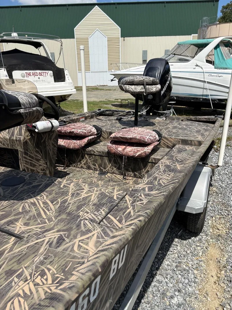 Slide: The Image of 2012 Crestliner 16 Ambush boat with camouflage design, parked on gravel near other boats. - 9