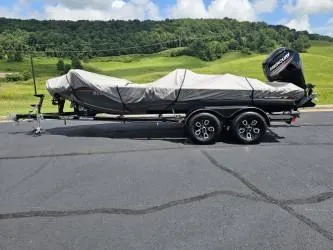 Slide: The Image of 2016 Tracker Pro Team 190 TX boat covered on trailer, parked on asphalt with scenic background. - 9