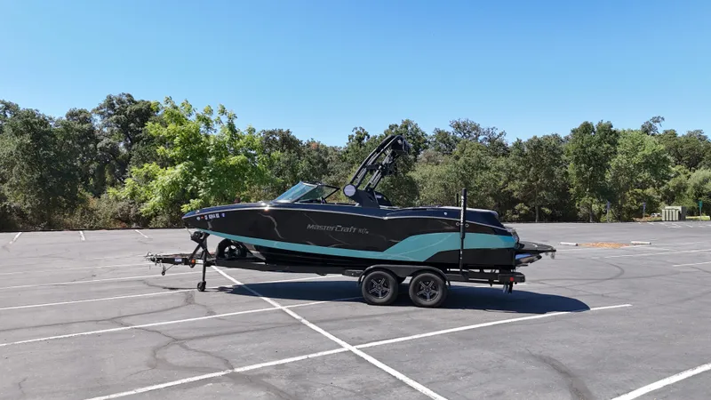 Slide: The Image of 2025 MasterCraft NXT22 boat on trailer in empty parking lot. - 2