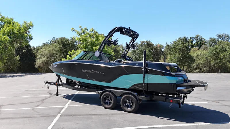 Slide: The Image of 2025 MasterCraft NXT22 boat on trailer in parking lot, surrounded by trees. - 3