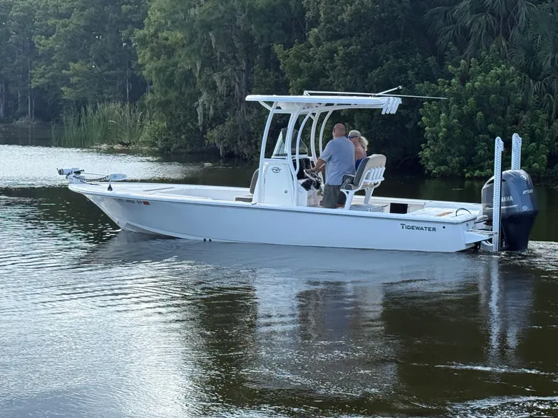 Slide: The Image of 2021 Tidewater 2410 Bay Max boat cruising on a calm river with lush greenery. - 0