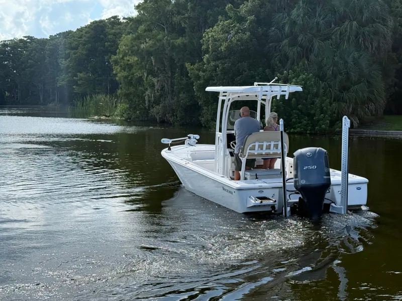 Slide: The Image of 2021 Tidewater 2410 Bay Max boat cruising on a serene lake with lush greenery. - 1