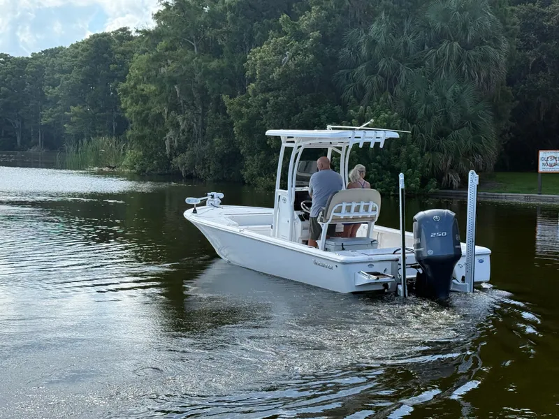 Slide: The Image of 2021 Tidewater 2410 Bay Max boat cruising on a serene lake with lush greenery. - 6