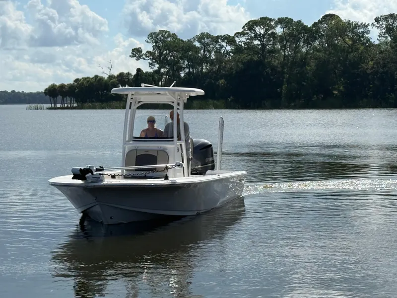 Slide: The Image of 2021 Tidewater 2410 Bay Max boat cruising on a serene lake with lush tree backdrop. - 8