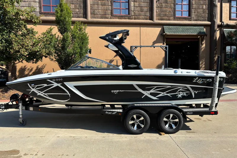 Slide: The Image of 2014 Tigé RZR boat on trailer, black with white graphics, parked outdoors. - 2